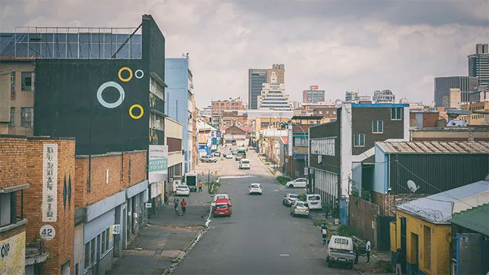 Urban street in an underrated travel destination, featuring cars and buildings under a cloudy sky.