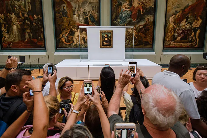 Crowd taking photos of the Mona Lisa at a hyped travel destination.
