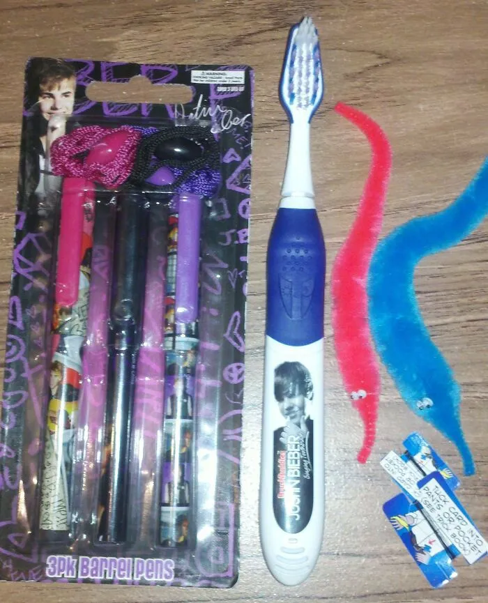Assorted disappointing gifts: branded pens, toothbrush, and colorful worm toys on a wooden surface.