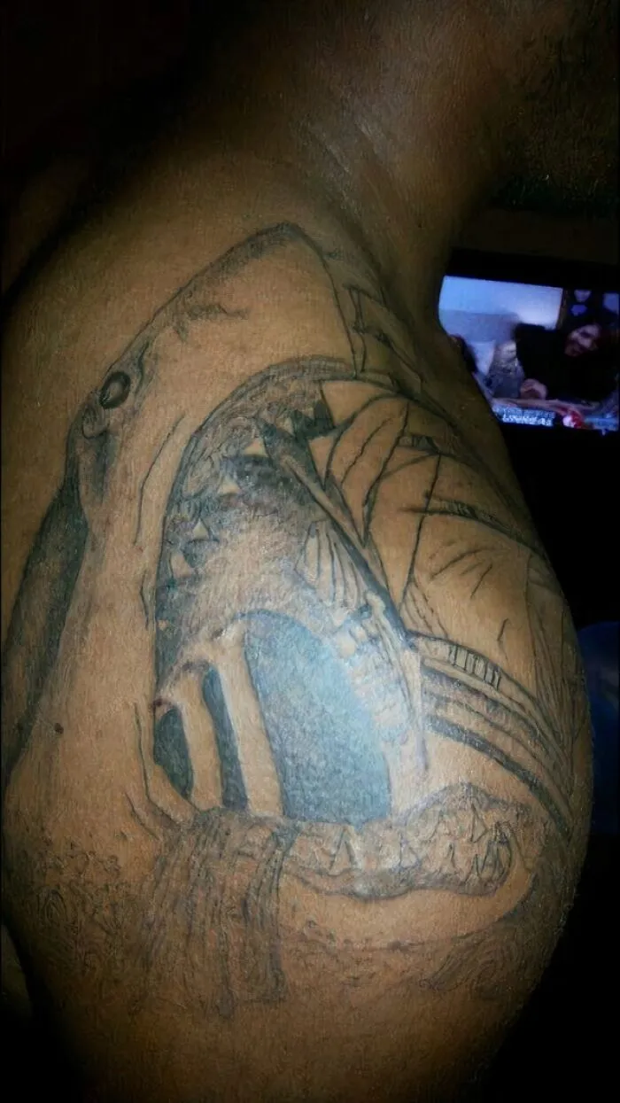 Poorly drawn shark tattoo fail on shoulder, showcasing unintended artistry mishap.
