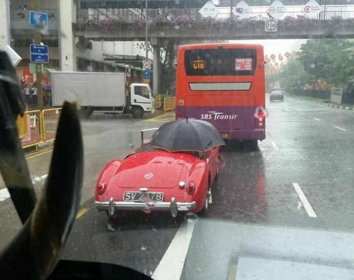 This Person Is Driving In The Rain While Holding An Umbrella
