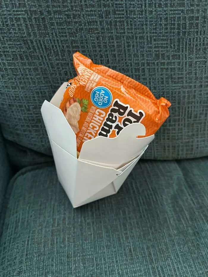 Ramen packet in takeout box on couch, symbolizing disappointing gift.