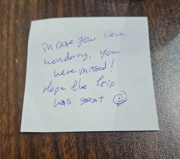 Handwritten note from a good funny boss saying "In case you were wondering, you were missed! Hope the trip was great" with a smiley face.