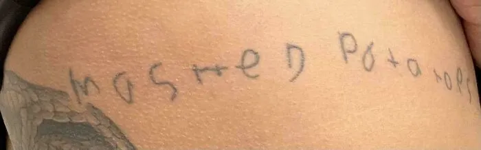 Hand-drawn funny worst tattoo fail spelling "mashed potatoes" with uneven letters on skin.