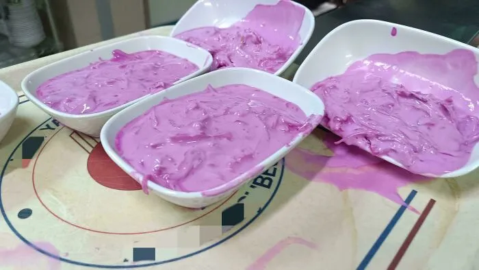 Four white bowls filled with a bright purple creamy dish, spilling over on a table, unusual dishes presentation.