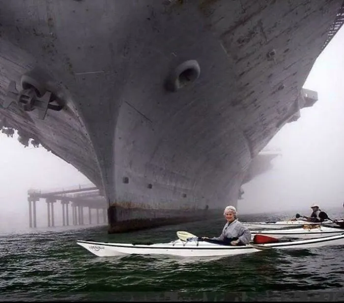 Kayakers paddling underneath a massive ship hull, showcasing an impressive example of megaphobia and scarily big objects.