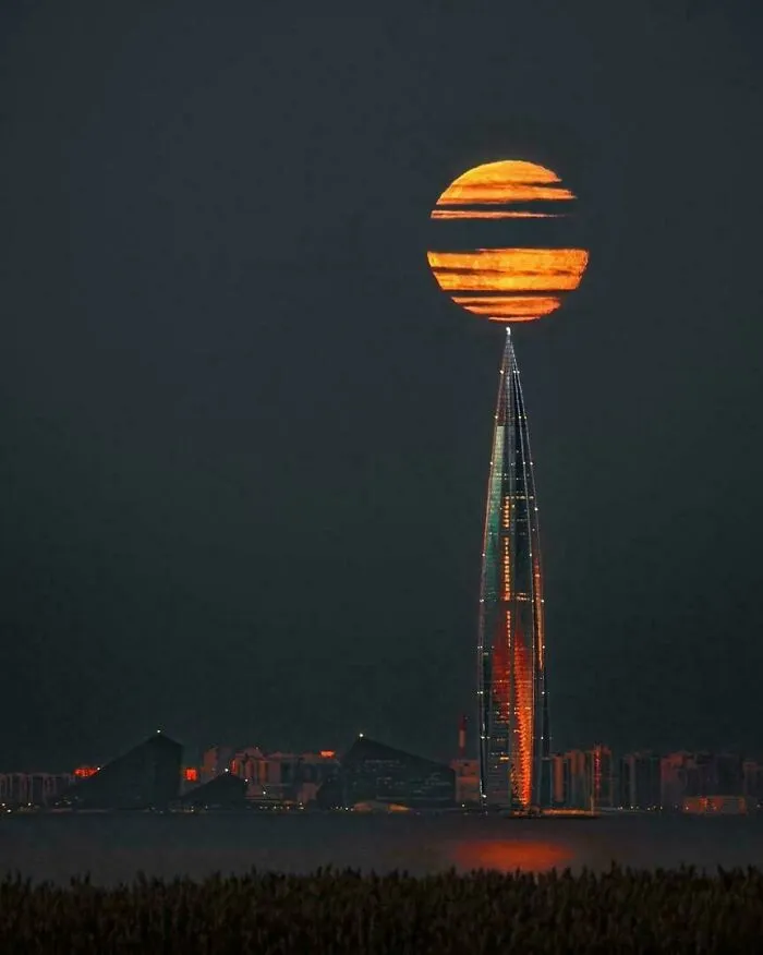 Massive full moon appearing above the tallest skyscraper at night, showcasing a scarily big natural phenomenon for megalophobia.