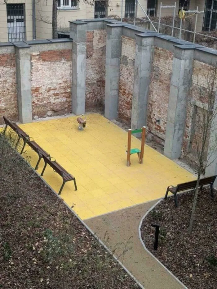 Área de «infierno urbano» con bancos y un solitario juego infantil rodeado de muros de ladrillo.