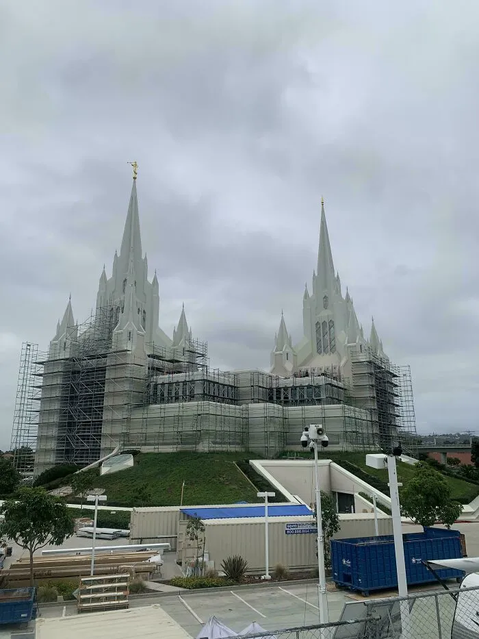 Gothic building under renovation with scaffolding, featuring sharp spires and an eerie atmosphere fitting supervillain headquarters.