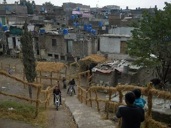 Calle ascendente en barrio urbano con casas de ladrillo y tanques de agua azules.