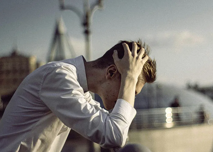 A stressed person in a white shirt sitting outdoors, representing regret over shared secrets.