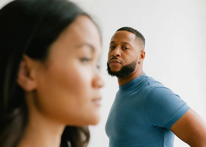 Man in blue shirt looking contemplative while standing behind a woman, illustrating secrets revealed.