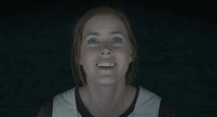 A woman with an engaging expression, representing a strong female protagonist in a dimly lit setting.