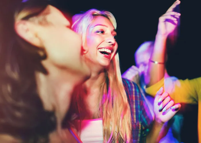 People laughing and dancing at a party, vibrant lights in the background.