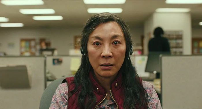 A woman in an office wearing headphones and a red vest, embodying a strong female protagonist in a determined expression.