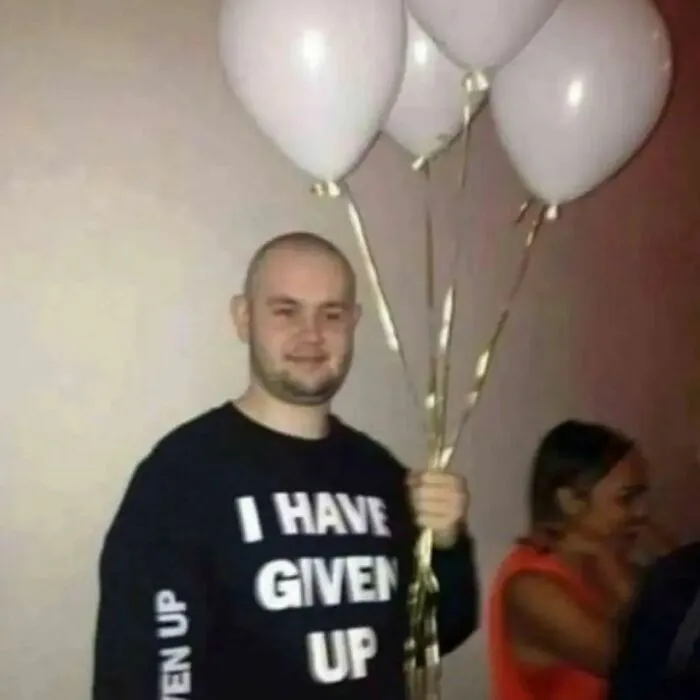 Person holding balloons, wearing a shirt that humorously reads "I have given up," reflecting relatable mental health memes.