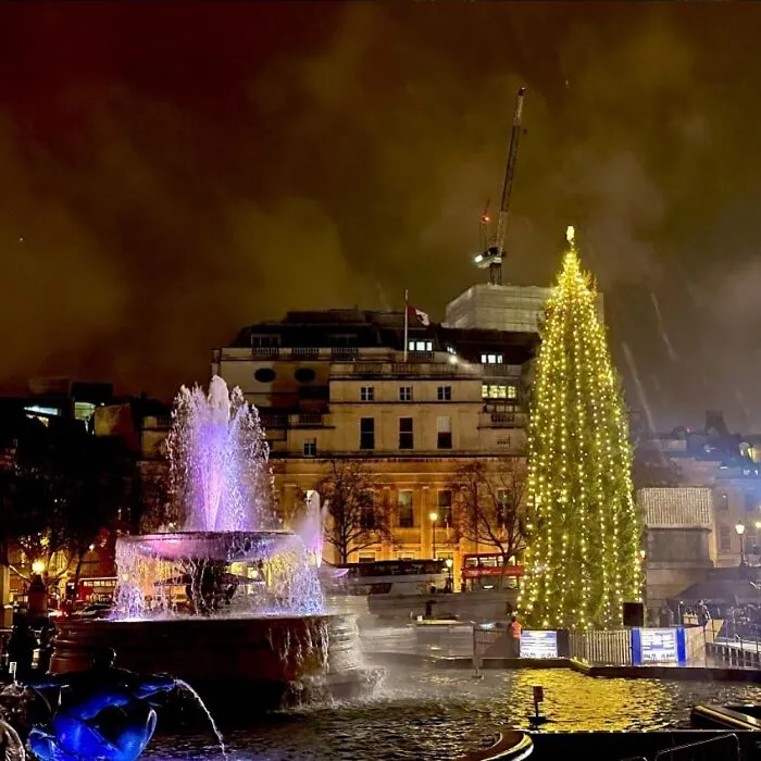 Illuminated Christmas tree in London city Trafalgar square with colorful fountain, showcasing global Christmas trees.