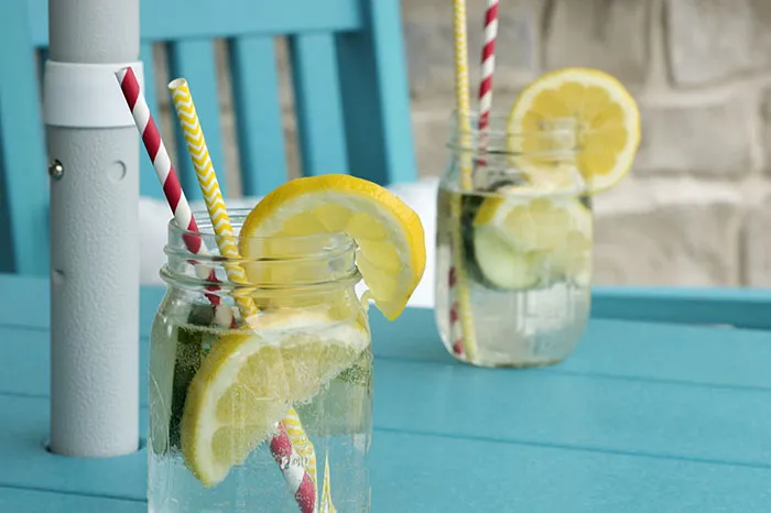 Two mason jars with lemon slices and striped straws on a blue table, showcasing refreshing crazy body life hacks.