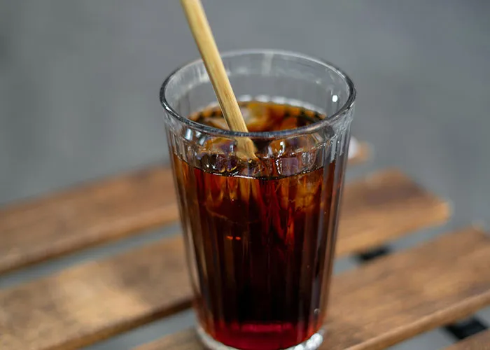 Glass of iced coffee with a bamboo straw on a wooden table, illustrating a creative frugal hack.