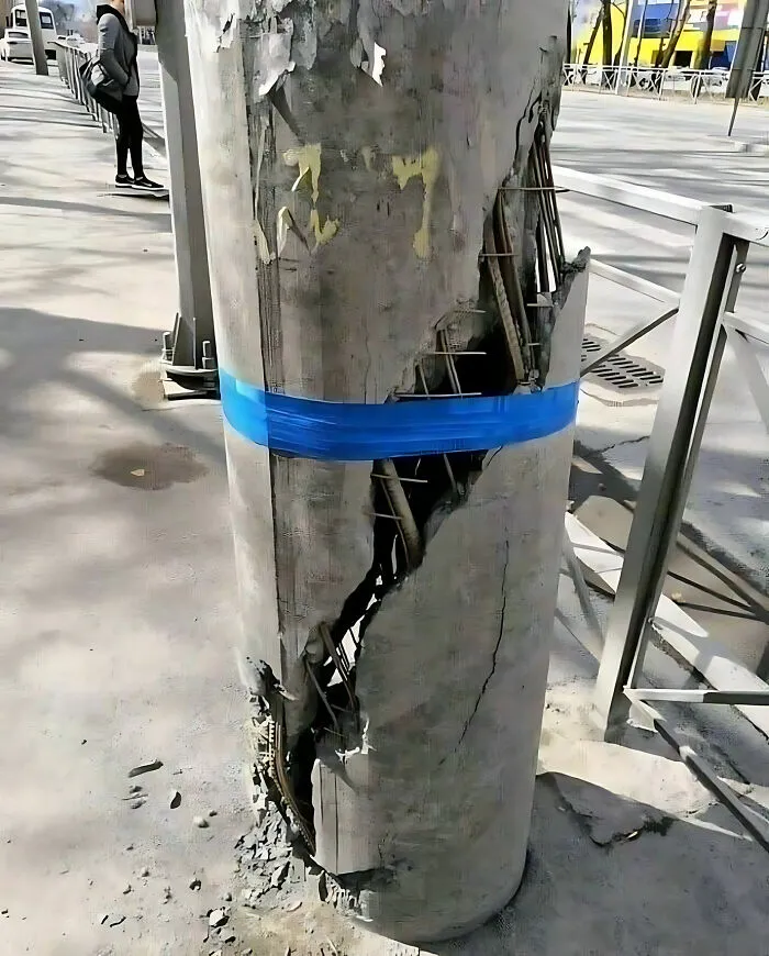 Damaged concrete pillar with exposed rebar and blue tape, illustrating a construction fail.