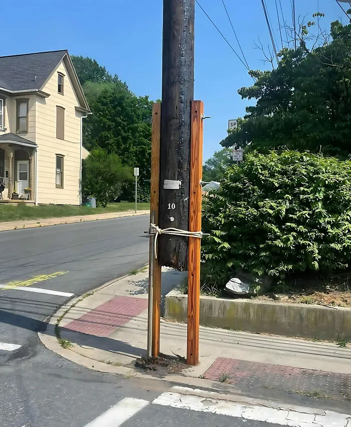 Utility pole awkwardly supported by wooden beams at a street corner, exemplifying a construction fail.