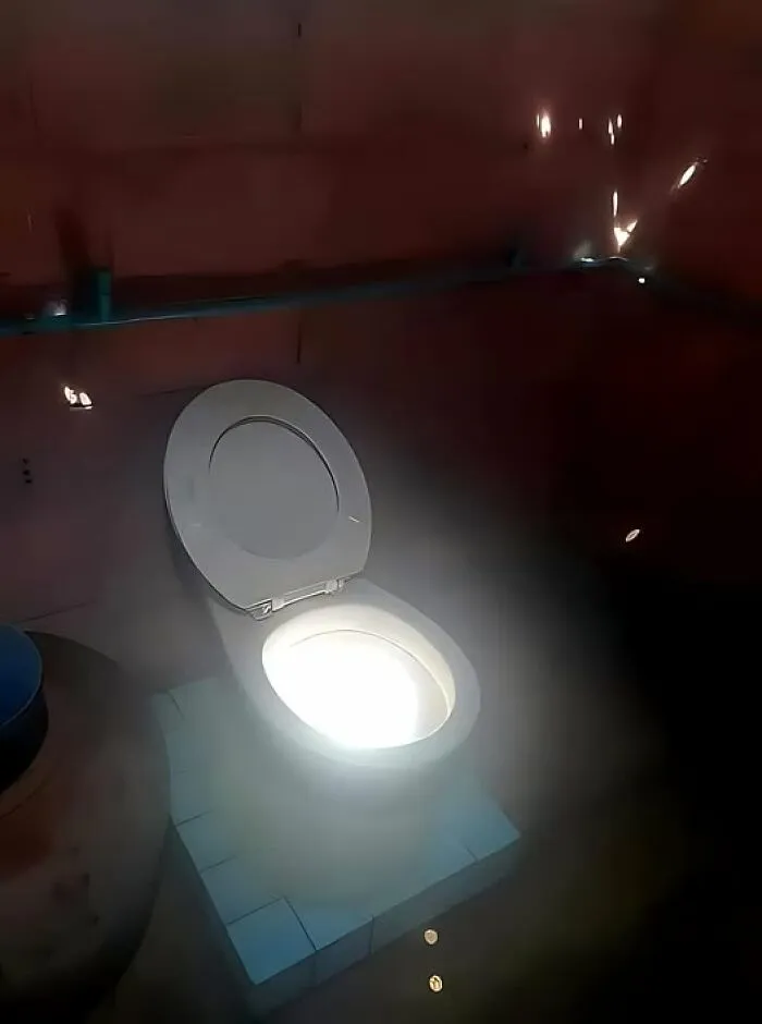 Illuminated toilet seat in a dimly lit room showcasing a humorous construction fail.