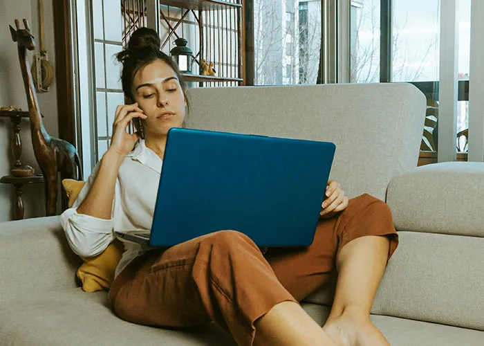 Woman on phone working on a laptop while sitting on a couch, symbolizing life-changing events and multitasking skills.