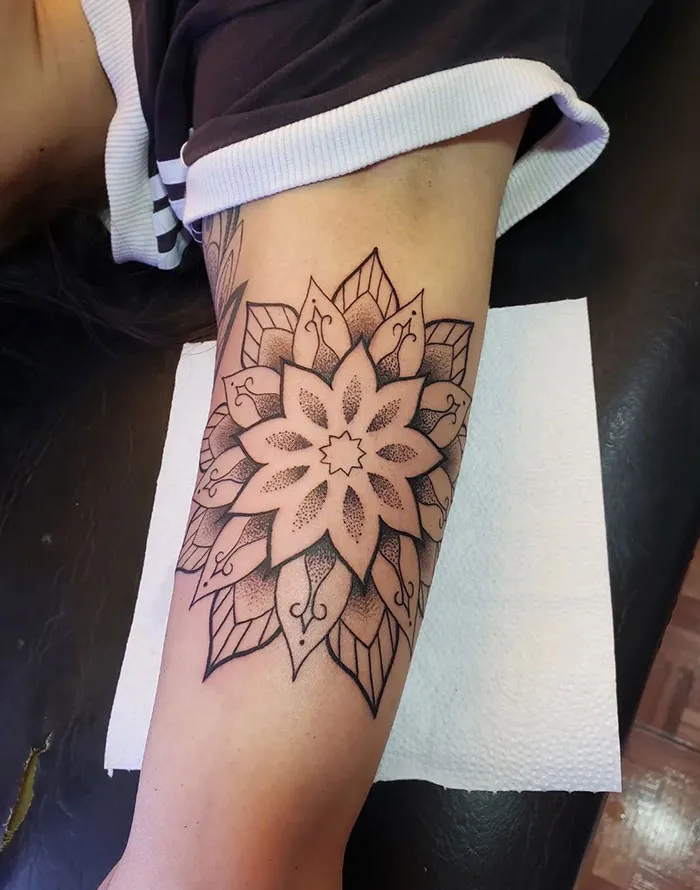 Intricate mandala tattoo design on inner arm, showcasing detailed patterns and shading.