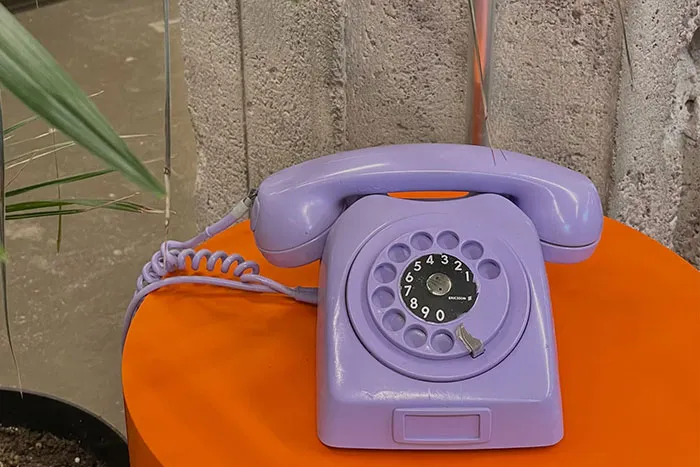 A vintage purple rotary phone on an orange table, symbolizing outdated technology.
