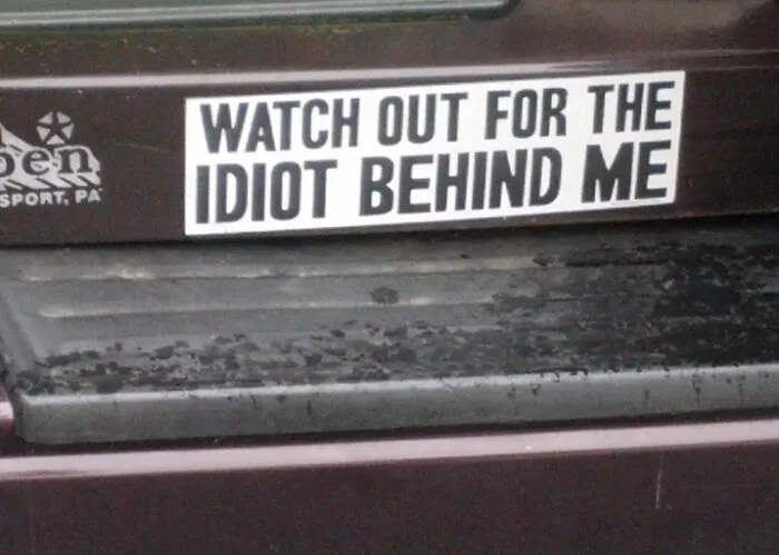 Bumper sticker reading "Watch out for the idiot behind me" on a car.
