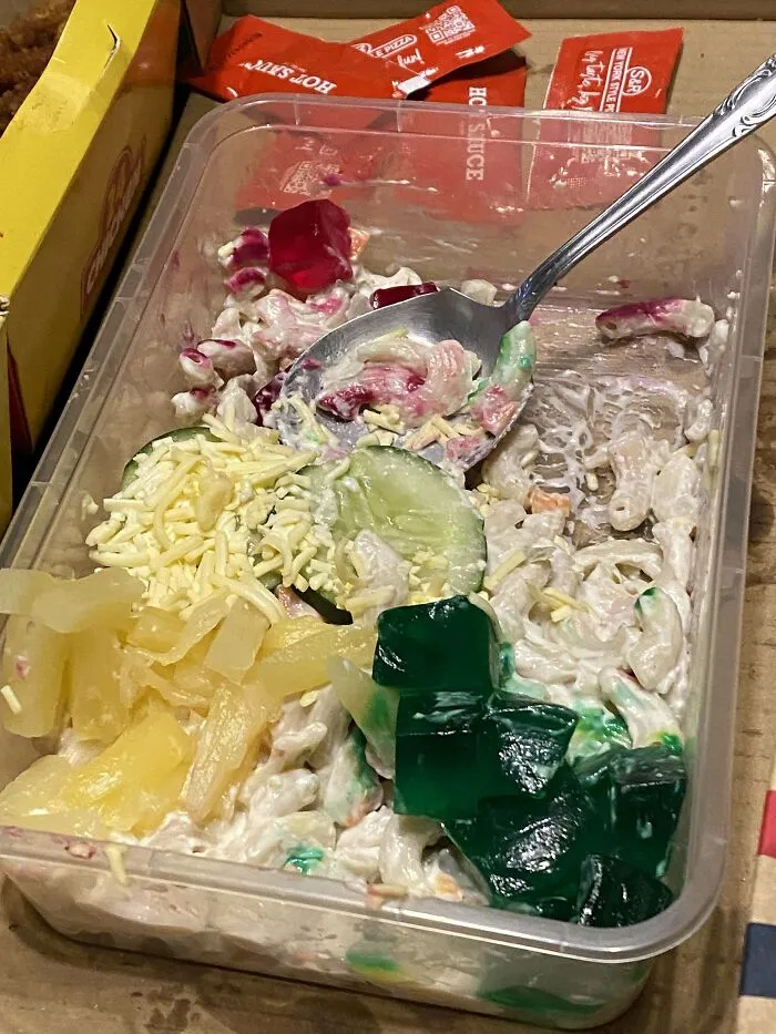 Macaroni salad with gummy bears, cucumbers, shredded cheese, pineapple, and hot sauce packets, an unusual dish combination.