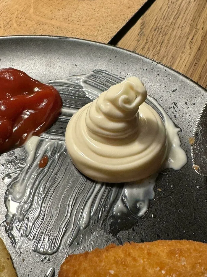 Swirled mayo resembling a soft-serve ice cream cone on a plate, with ketchup beside it.