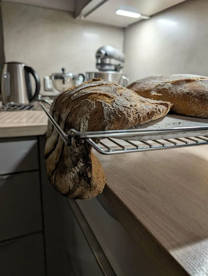 Pan artesanal con forma inusual enfriándose en la rejilla en una cocina moderna, llevándolo a otro nivel de repostería.