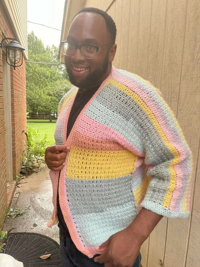 Person smiling in a colorful crocheted cardigan outdoors.