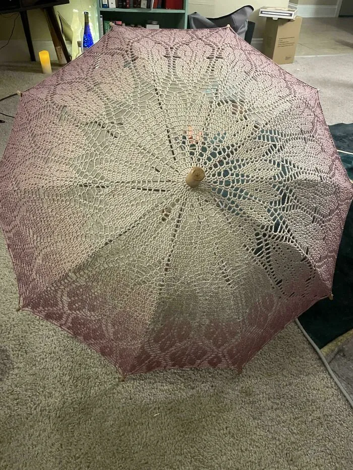 Crocheted parasol with intricate lace pattern on display indoors.