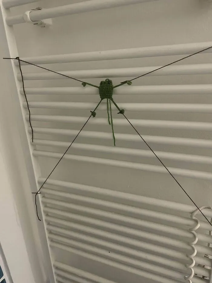 Crocheted green spider with string legs on a white radiator.