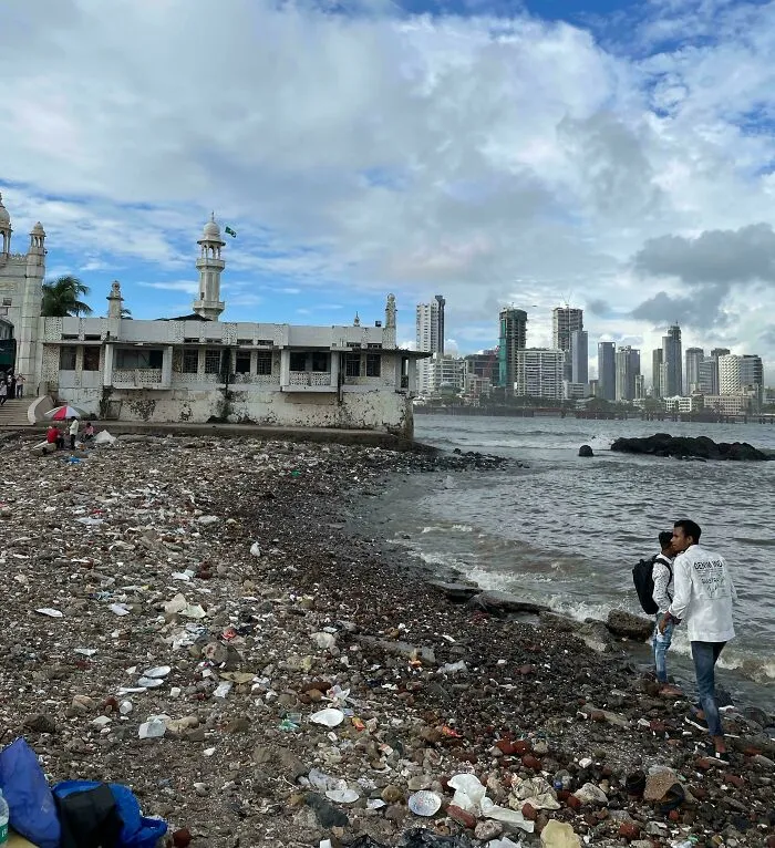 Playa en ciudad con basura y edificios, reflejando el «infierno urbano» construido por humanos.