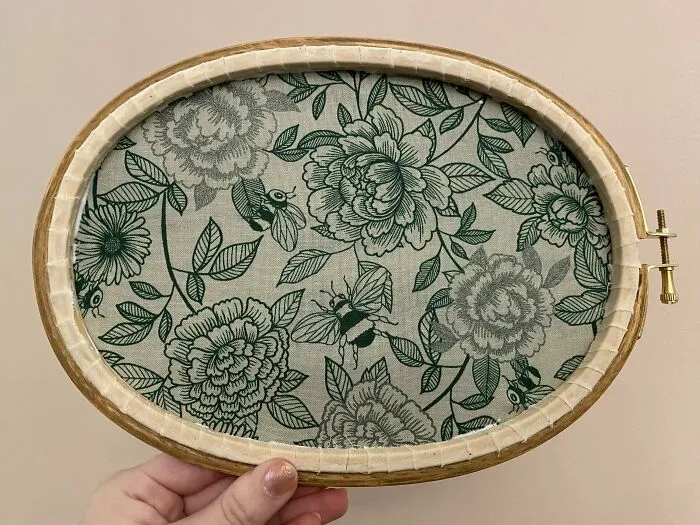 Hand holding embroidery hoop with beautiful floral and bee embroidery designs on fabric.