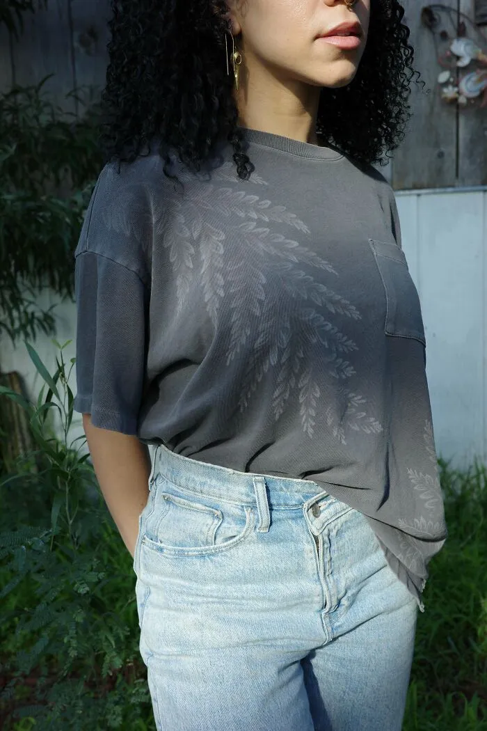 Curly-haired woman in a DIY printed gray shirt and jeans, standing in a garden.