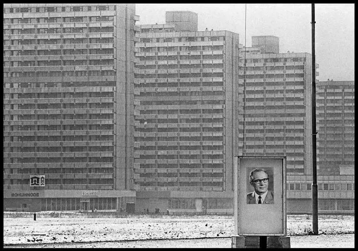 Large brutalist buildings with cold, uniform architecture evoke supervillain headquarters vibes in a stark, snowy urban scene.
