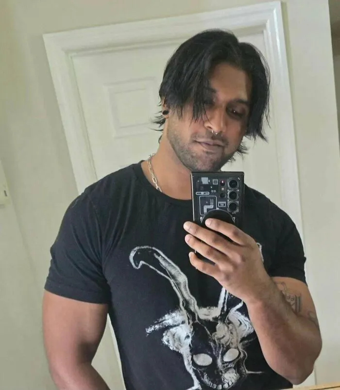 Man with fierceflow beautiful hair taking a mirror selfie, wearing a black graphic t-shirt with tattoos visible.