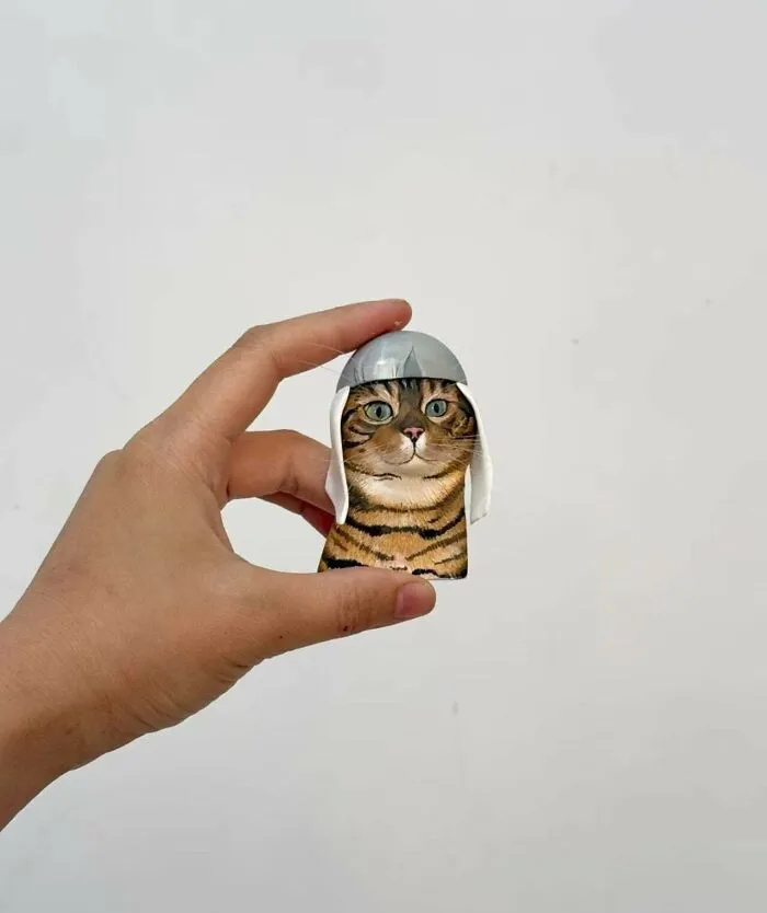 Hand holding a tiny DIY project: a cute figurine of a cat wearing a helmet.