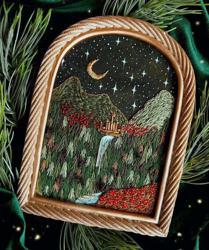 Embroidered mountain landscape with a waterfall and crescent moon surrounded by green pine branches and velvet fabric.
