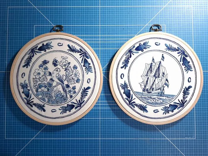 Two blue and white embroidery designs featuring a bird and a sailing ship, displayed on a grid background.