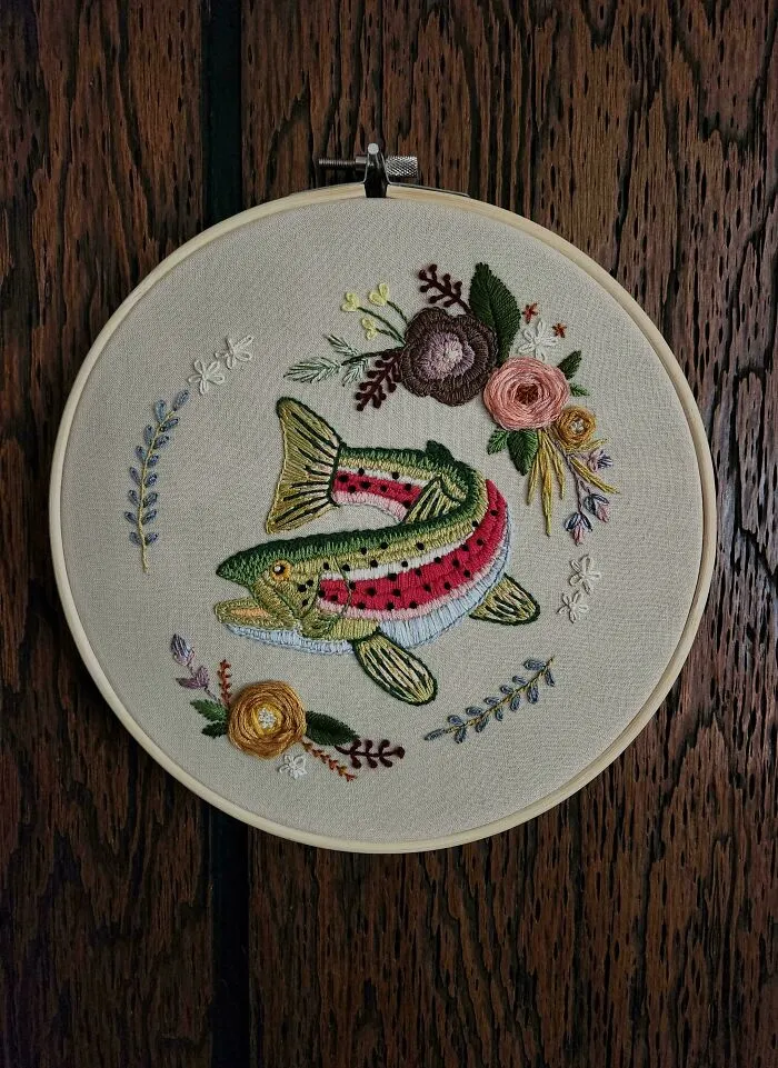 Embroidery hoop with colorful fish and floral designs showcasing beautiful embroidery skills on fabric.