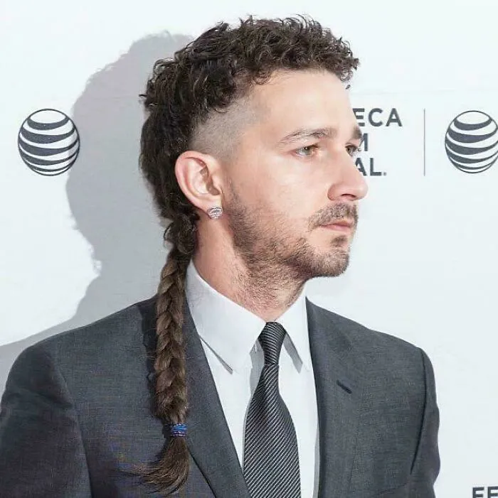 Shia LaBeouf with an unfortunate haircut featuring shaved sides, curly top, and a long braided rat tail.