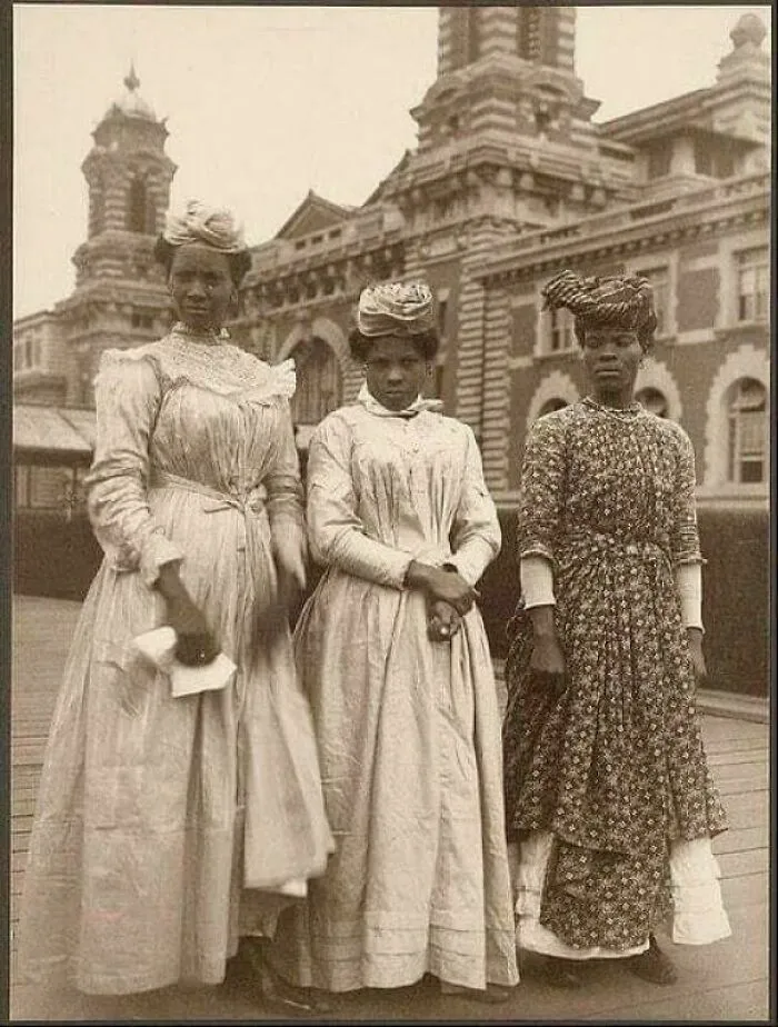 Victorian era women in period dresses posing outdoors in front of a historical building.