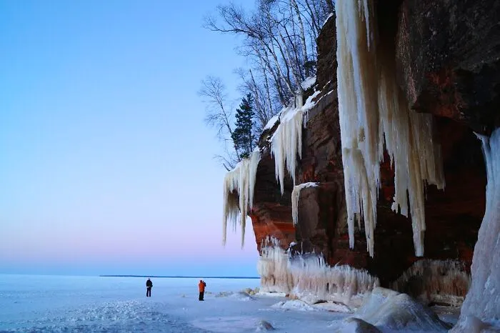 Amazing views with ice formations and two people exploring a frozen landscape beneath towering cliffs.