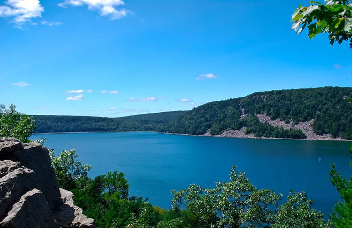 Scenic view of a blue lake surrounded by lush green forests and hills under a clear sky, representing amazing views in states.