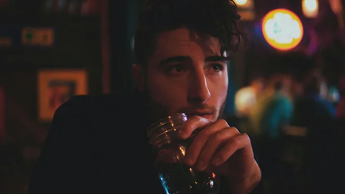 Man at a bar with a drink, pondering dark secrets while intoxicated.